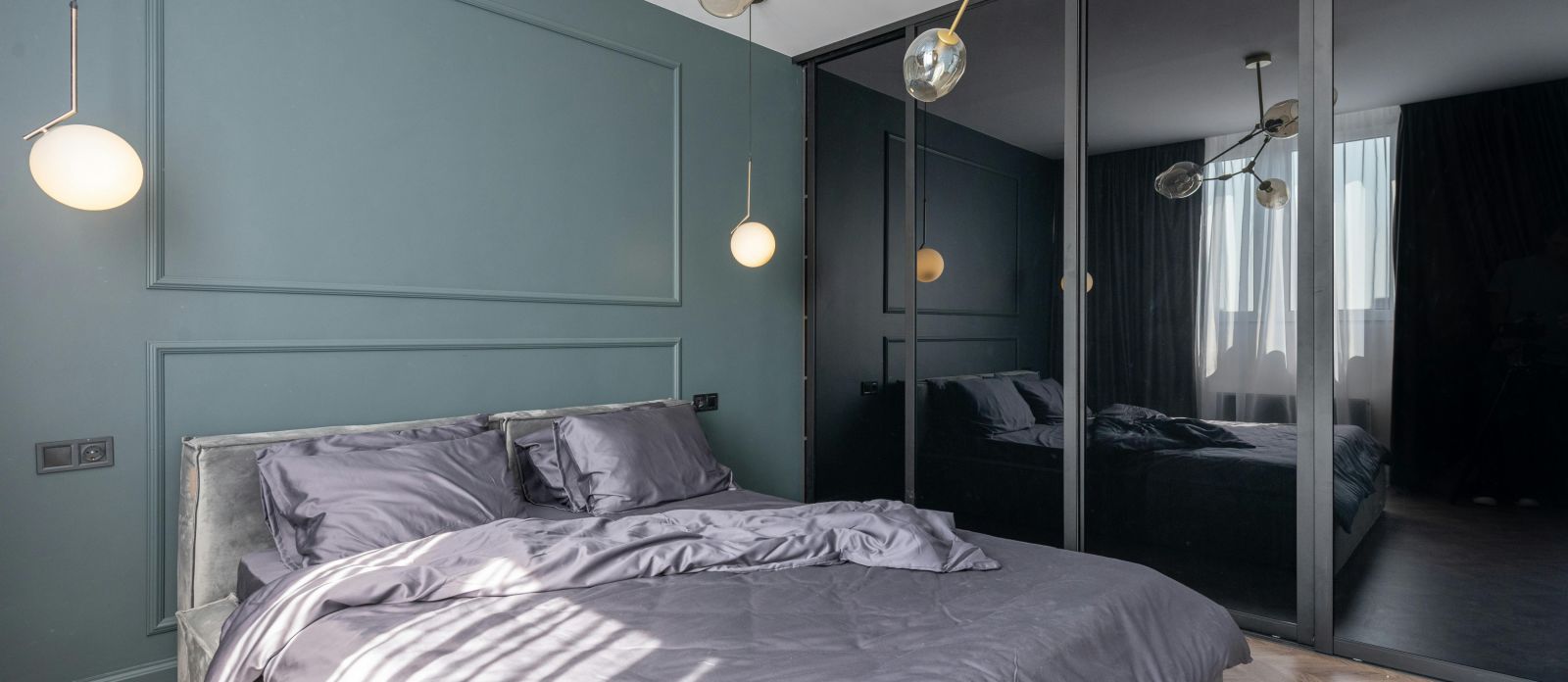 image of a modern bedroom with teal coloured master wall featuring a plush bedding in the middle with black panel wardrobein the corner of the room