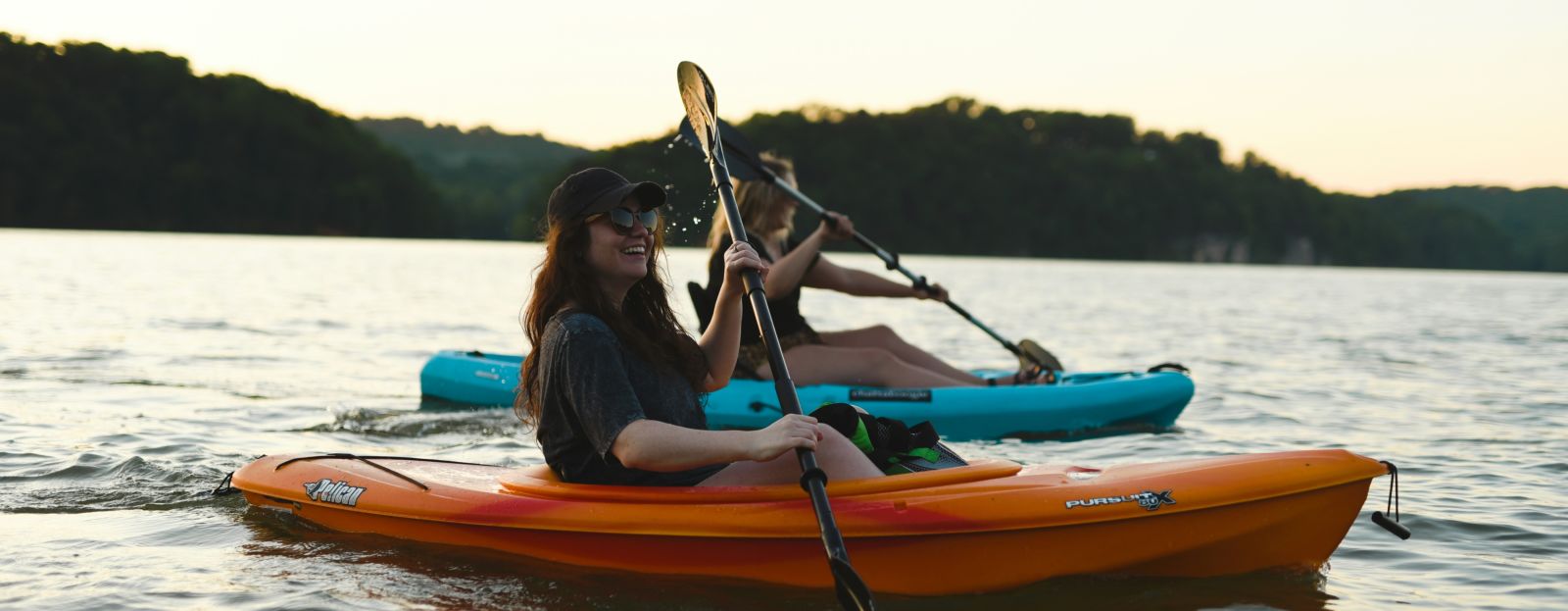 two women kayaking on a waterbody with mountains in the background