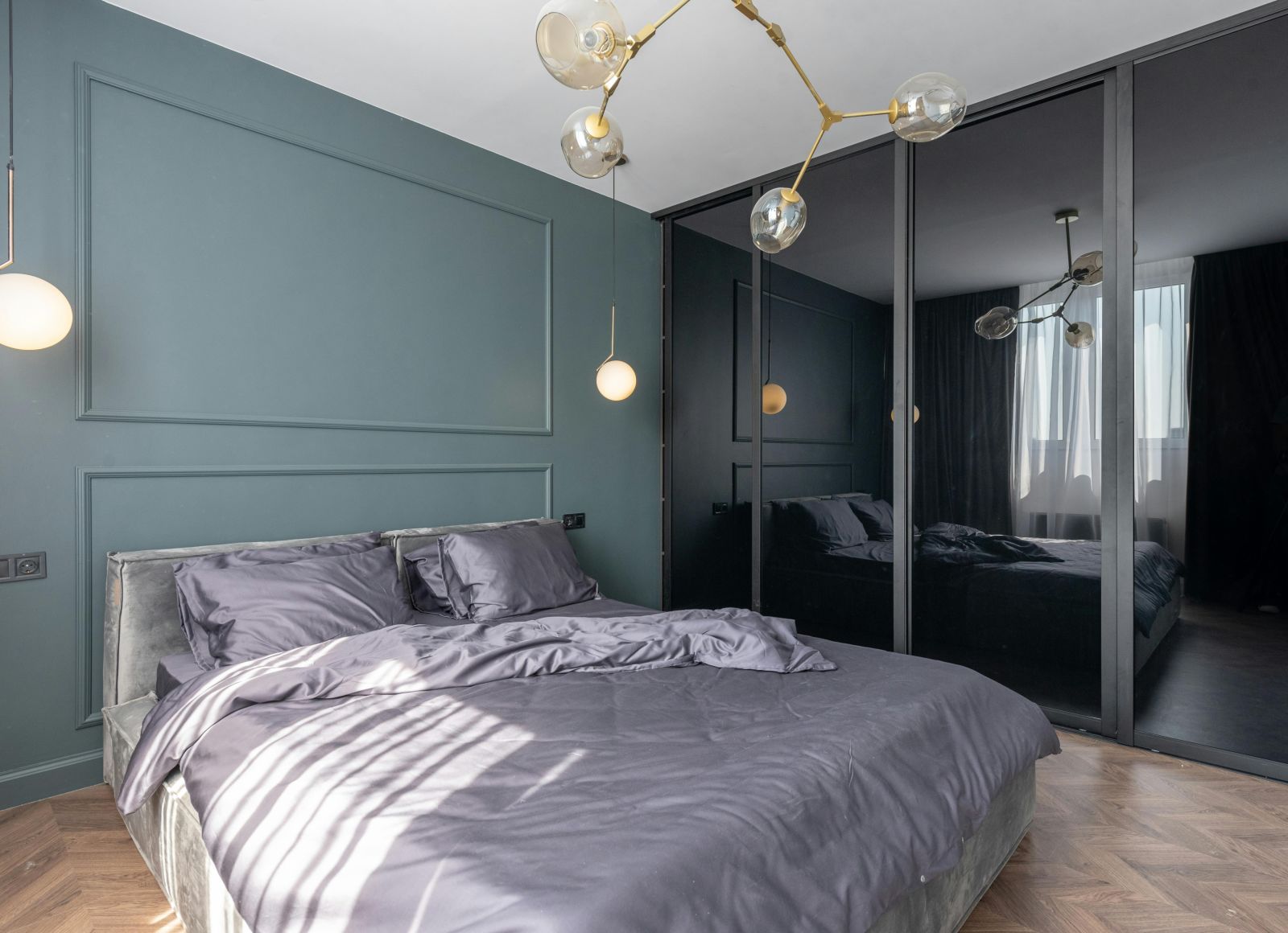 image of a modern bedroom with teal coloured master wall featuring a plush bedding in the middle with black panel wardrobein the corner of the room