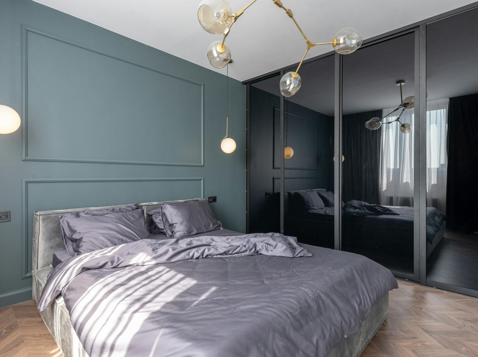 image of a modern bedroom with teal coloured master wall featuring a plush bedding in the middle with black panel wardrobein the corner of the room