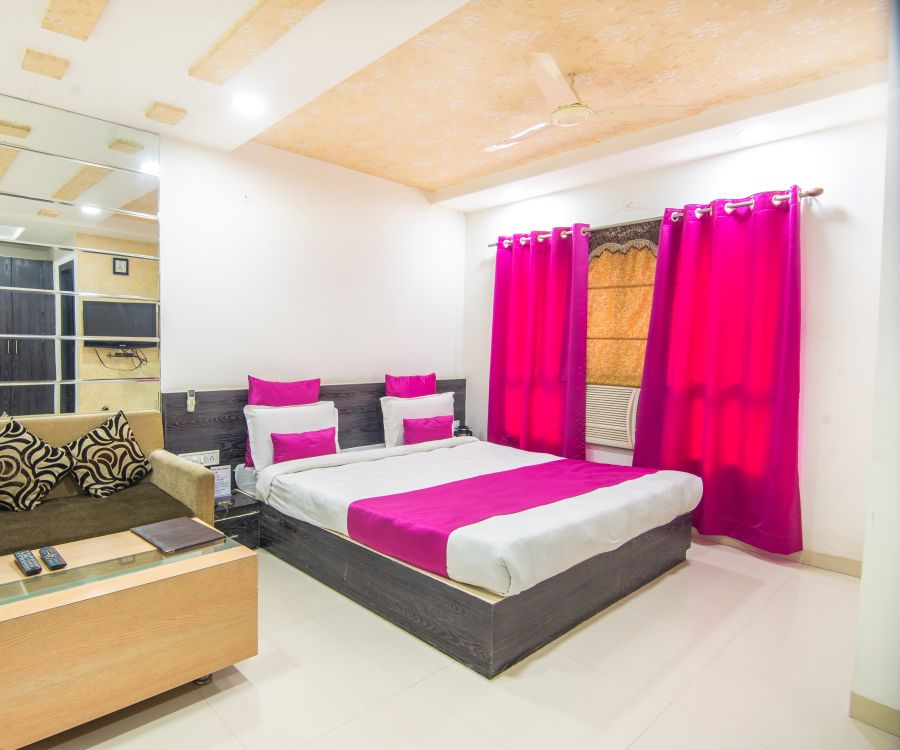 alt-text A room with a sofa bed, decorative pillows, a coffee table and violet curtains -  Morya Regency, Bhopal