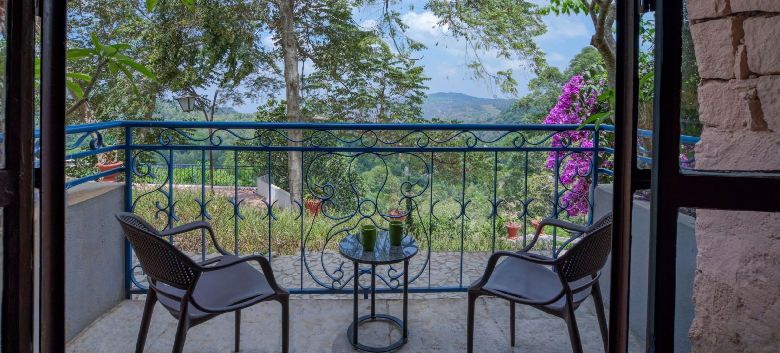 Balcony with two chairs and a table, overlooking a lush green landscape and vibrant flowers. | Mango Hill, Yercaud