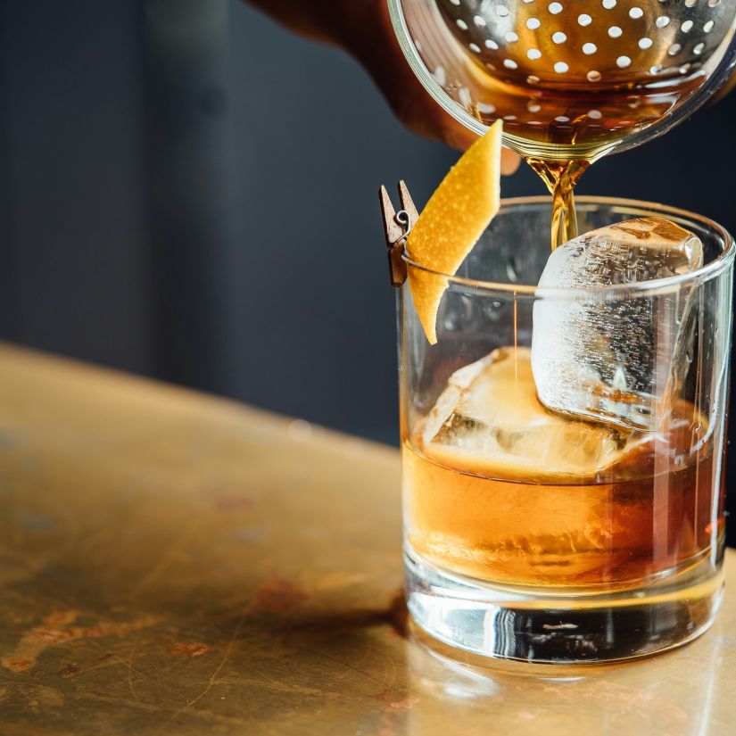 A drink being poured to a glass with ice inside it