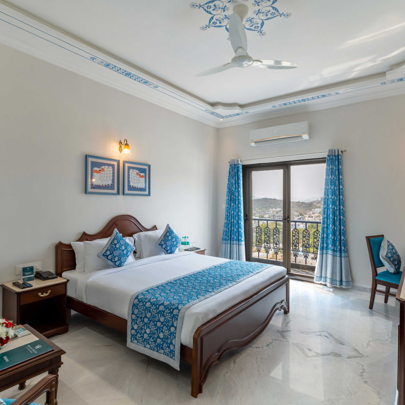 King bed with blue runner and blue curtains inside Deluxe Room - Maan Vilas by Stone Wood, Udaipur