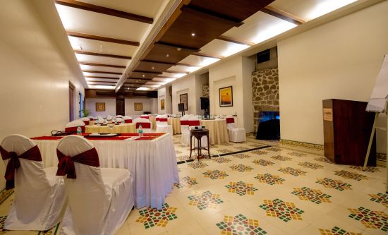 alt-text Conferance hall with white covered chairs and blue linen covered table at Fort JadhavGADH