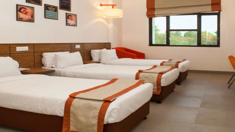 A spacious comfy room with 3 plushy bed, posters on wall, an open window at Max Hotel Prayagraj.
