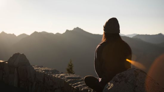 silhouette of woman sitting on a mountain peak