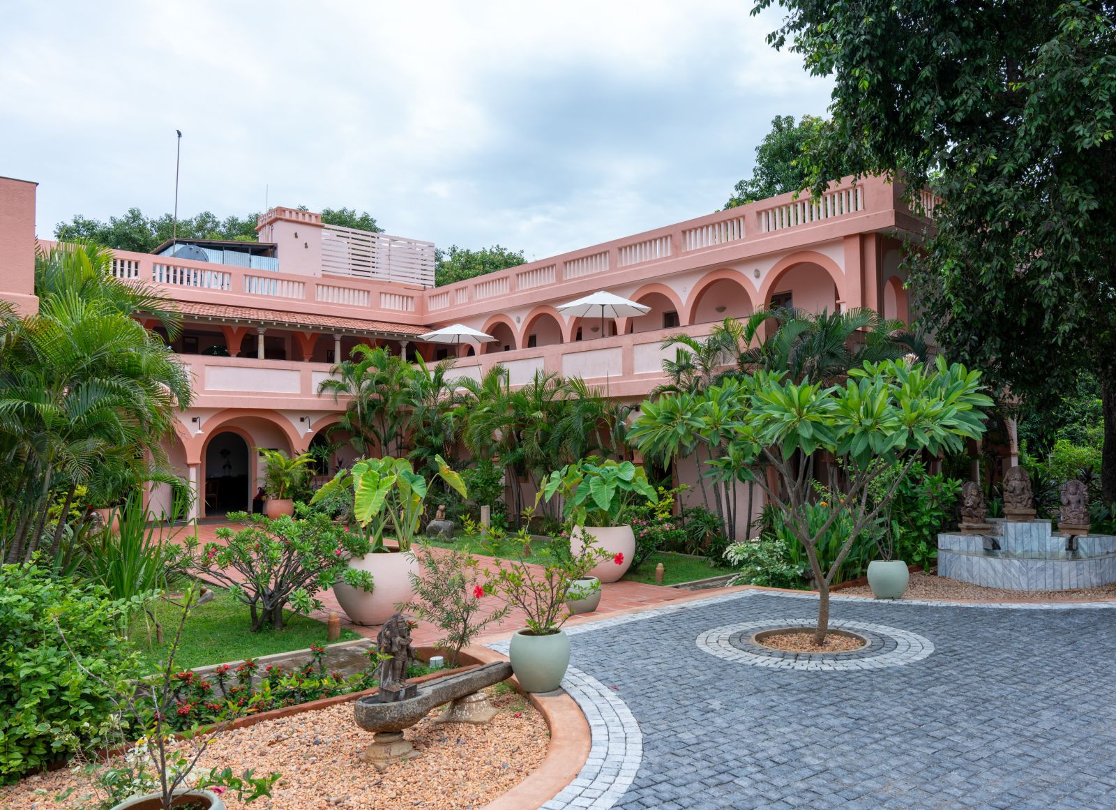 Pathway of a resort with a tree in the middle of it and a backdrop of sky with clouds.