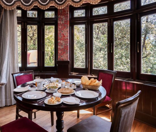 alt-text A dining space with chairs, large windows overlooking a forest and a table adorned with various snacks - 