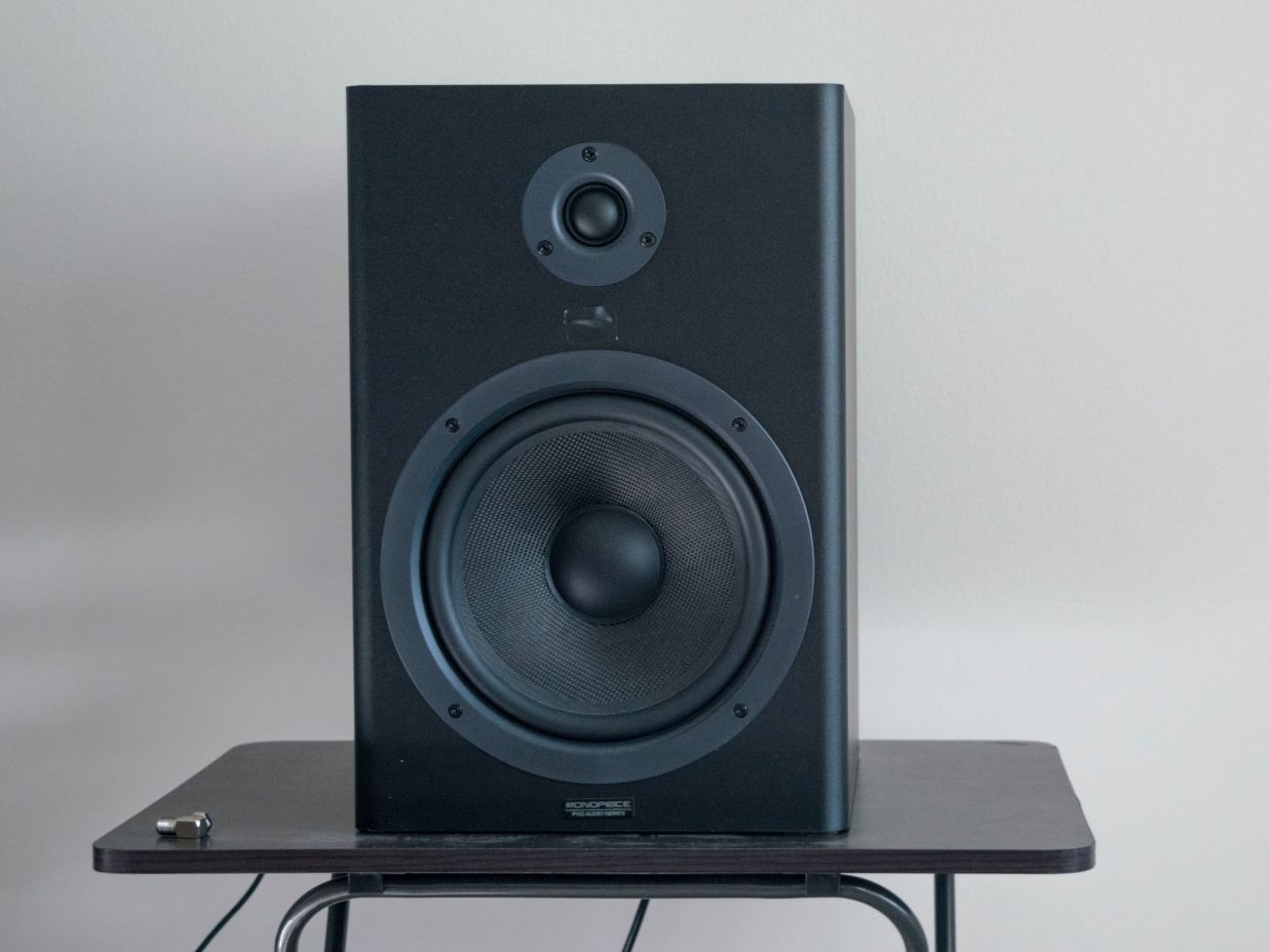 Image of a speaker placed on a small table with a white coloured wall in the background