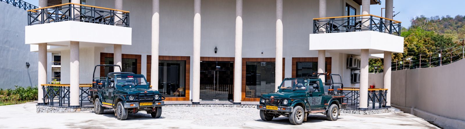 A facade image of the hotel with two jeeps in front seen on a sunny day - Shervani Pebbles & Pines, Corbett