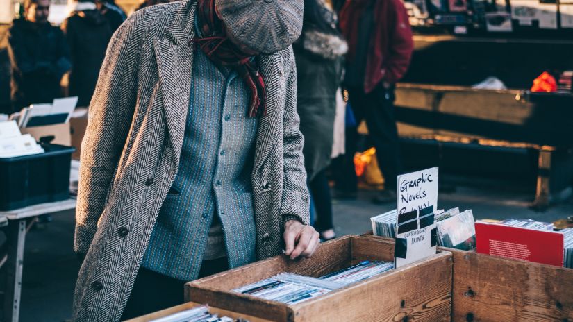 a person looking at novels that is placed inside a box during a flea market