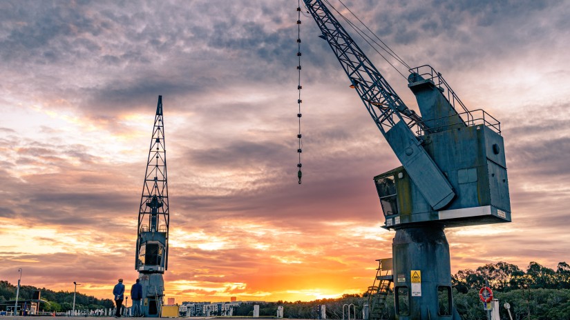 A long shot of 2 static cranes with a backdrop of purple sky and golden sunset