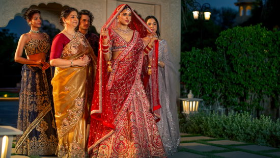 alt-text Four women in traditional indian sarees pose together at dusk, with soft lighting and a garden in the background.