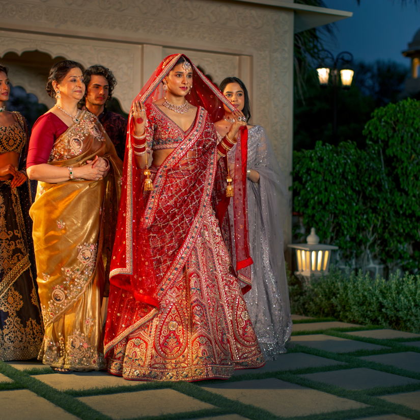 Four women in traditional indian sarees pose together at dusk, with soft lighting and a garden in the background.