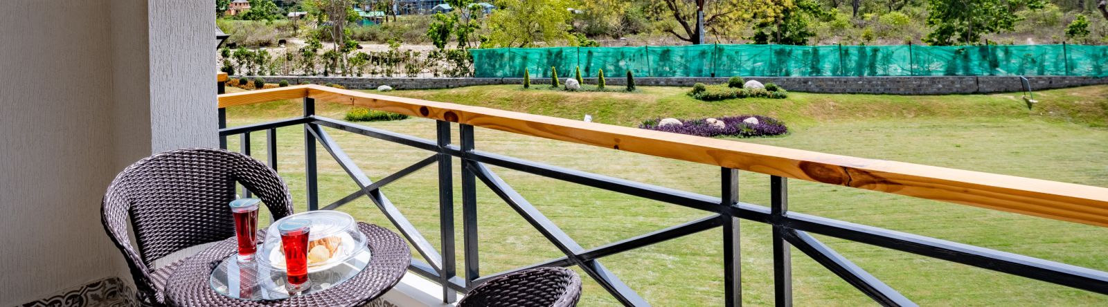 A balcony in the river view room with comfortable chairs placed around a coffee table for relxation - Shervani Pebbles & Pines, Corbett