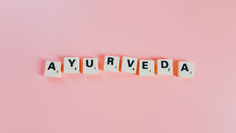 Ayurveda written in scrabble tiles that is placed in a pink table