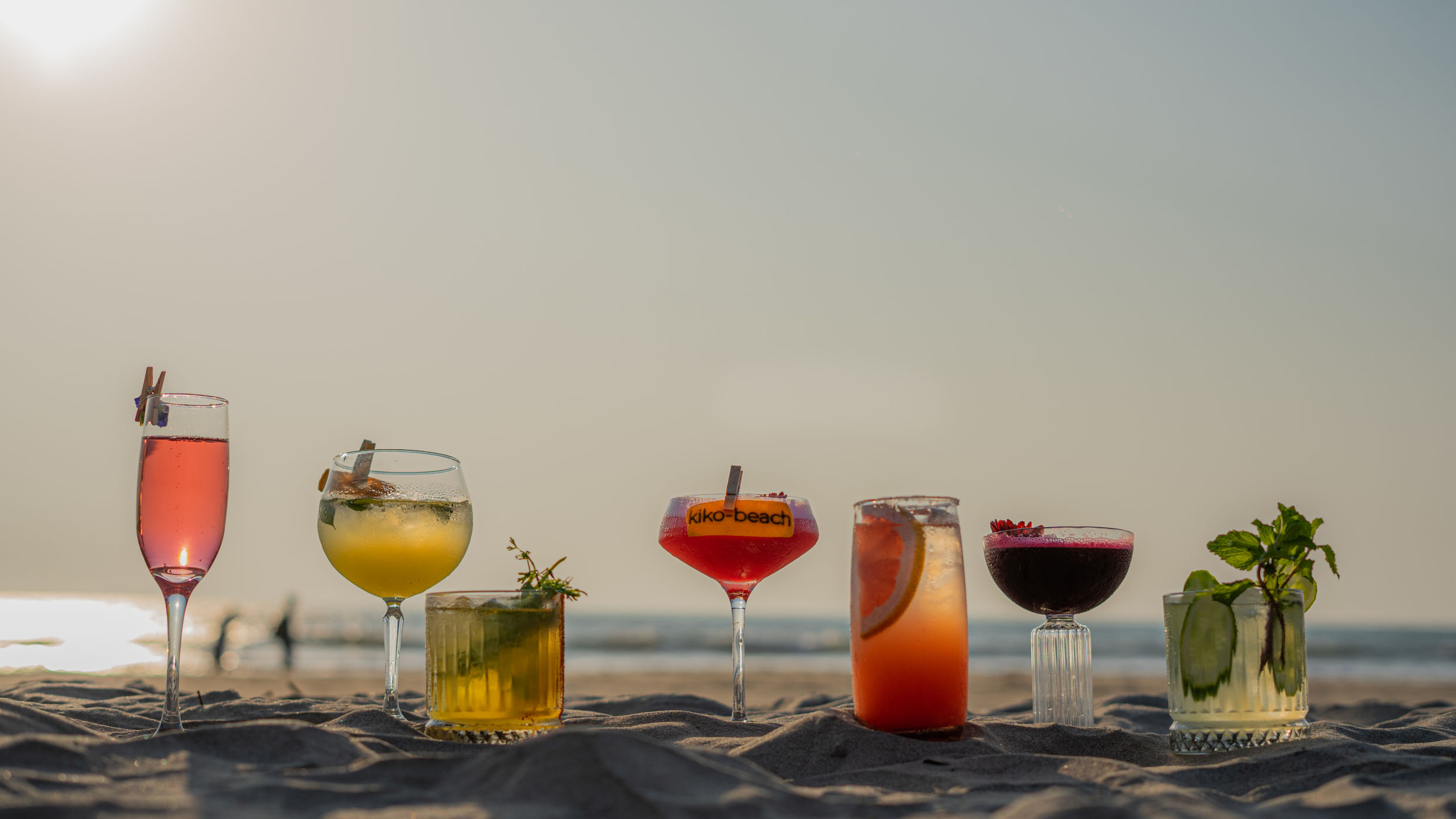 an image of a few cocktail glasses placed atop sand on a beach