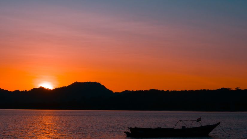 a boat on a water body with a sunrise over a hill in the backdrop