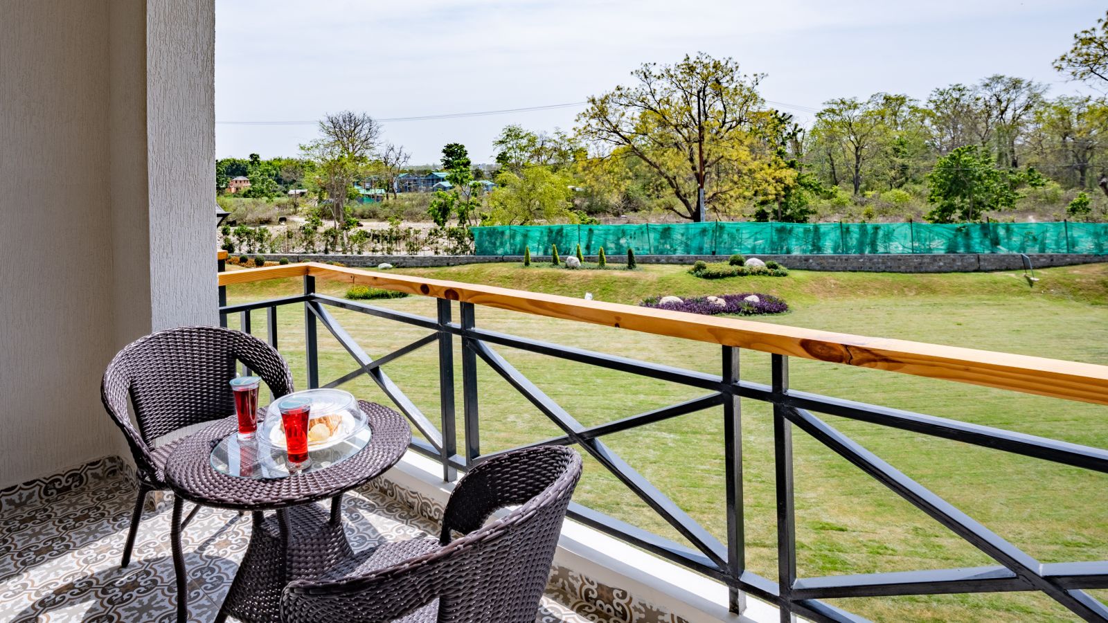 A balcony in the river view room with comfortable chairs placed around a coffee table for relxation - Shervani Pebbles & Pines, Corbett