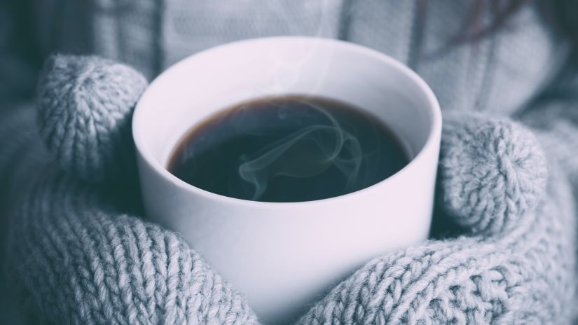 guest holding a cup of coffee with gloved hands