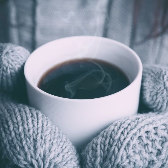 guest holding a cup of coffee with gloved hands