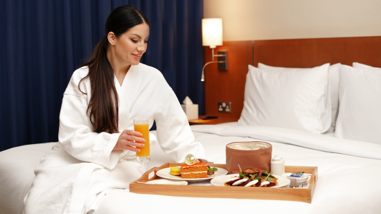 a woman sitting on a hotel bed with a tray filled with food items - La Maison Hotel, Doha