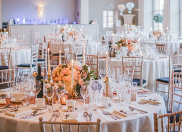 Image of a banquet hall with round tables neatly covered with wine and wine glasses