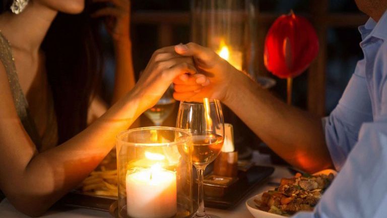 Couple holding hands at a candlelit dinner on a table