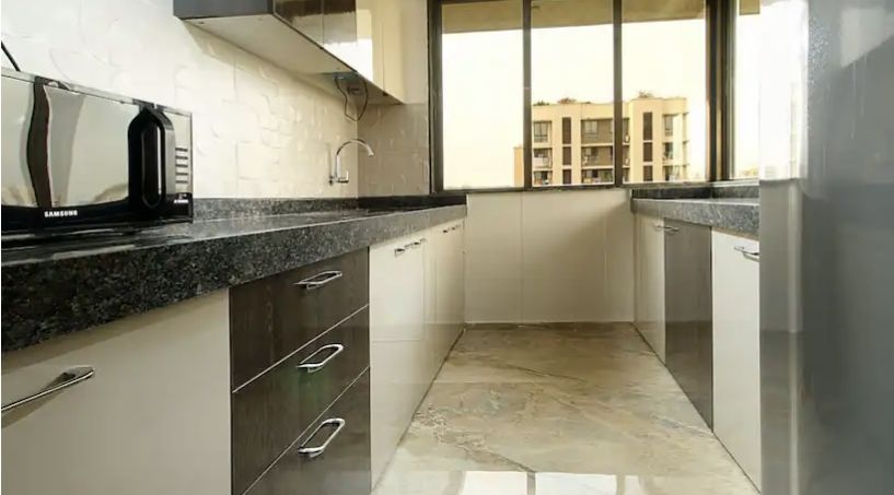 A modern kitchen with sleek cabinetry, granite countertops, a microwave, and a window that brightens the narrow space.