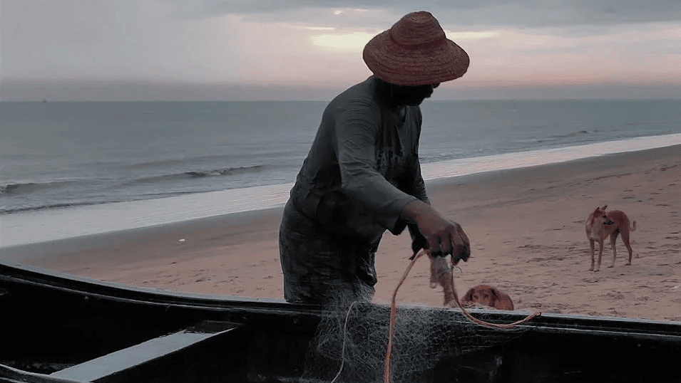 A man standing beside a boat by the beach fixing his fishing net