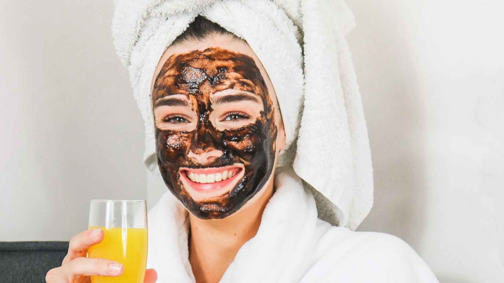 a woman with a face mask in bathrobe holding a glass of juice 