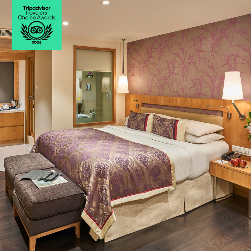 A luxurious hotel room with a double bed, purple and gold bedding, a seating area, and elegant decor. Tripadvisor Travelers' Choice Awards 2024 badge displayed.