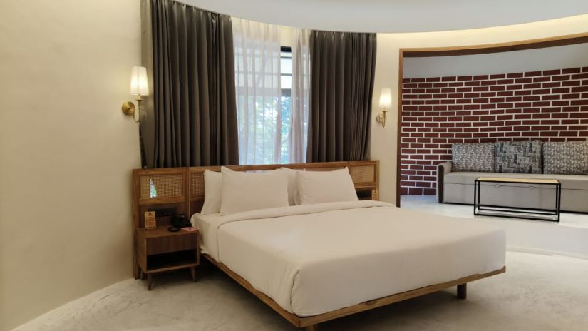 A dramatic brick feature wall, rich draperies, and a fluffy white bed define an opulent bedroom - Jagira Ananta Elite Gir