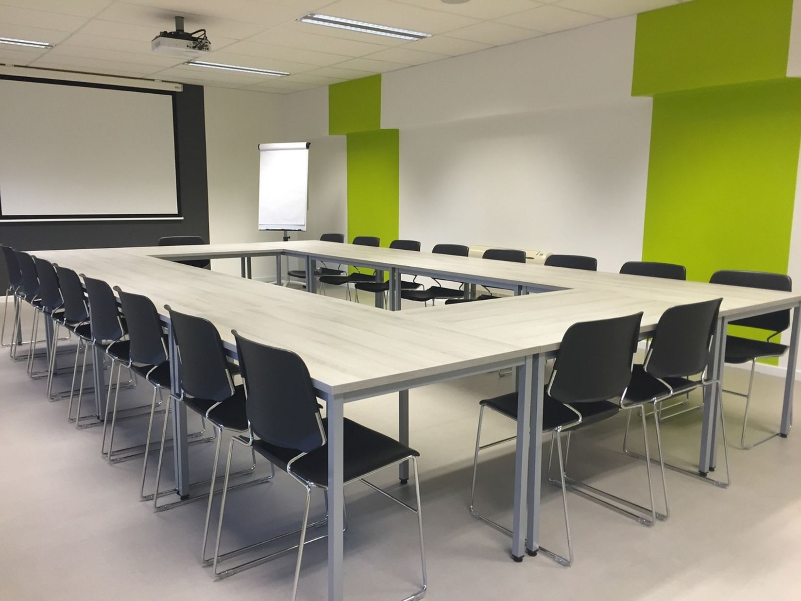 A seating area with multiple chairs a big table and a projector