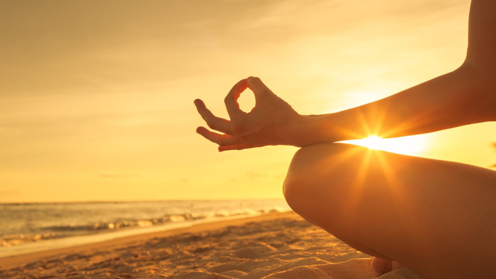 A person meditating on the beach at sunset.