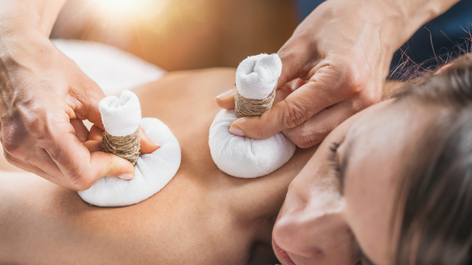 A person receiving a back massage with herbal compresses.