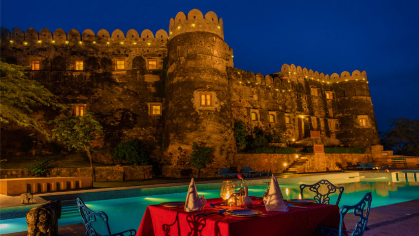 Hill Fort Kesroli 14th Century Alwar - image of a table with chairs facing the property's pool and the walls of the fort 