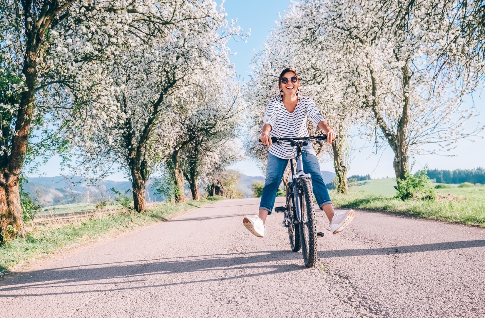 A woman riding a bicycle in an empty road with trees around