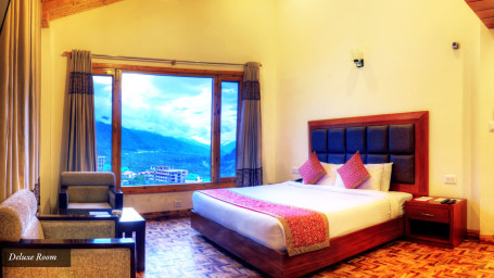 Deluxe room with seating area, bed and large window overlooking the valley at Summit Chandertal Regency Hotel & Spa