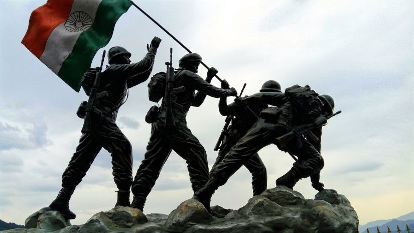 Four soldiers standing on a rock waving the Indian Flag