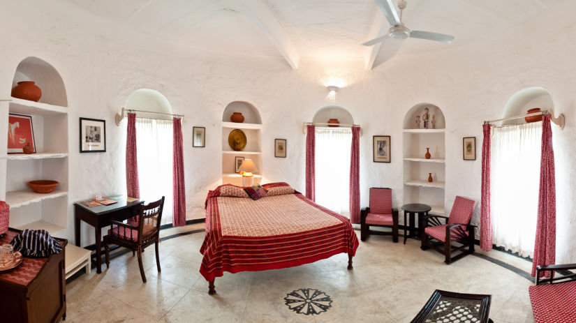 interior view of the Mubarak Mahal room with a queen size bed, a ceiling fan, several chairs and paintings on the wall