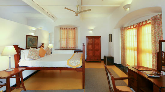 The Tower House - The Menezes room with a yellow curtains and a lamp table next to the queen size bed. The room also features a ceiling fan and a wooden wardrobe