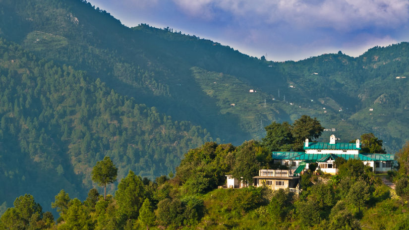 Facade of The Ramgarh Bungalows perched on a hill surrounded by scenic mountain view captured during the day