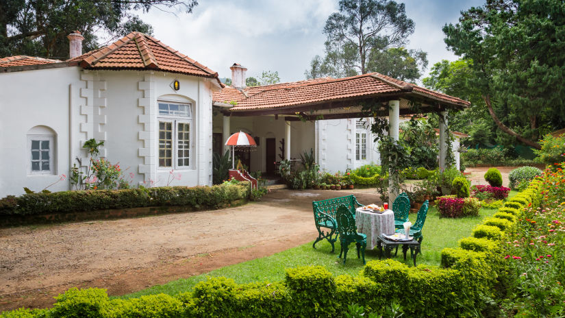 Facade of the hotel with mental chairs & a small table in the garden in front - Wallwood Garden - 19th Century, Coonoor