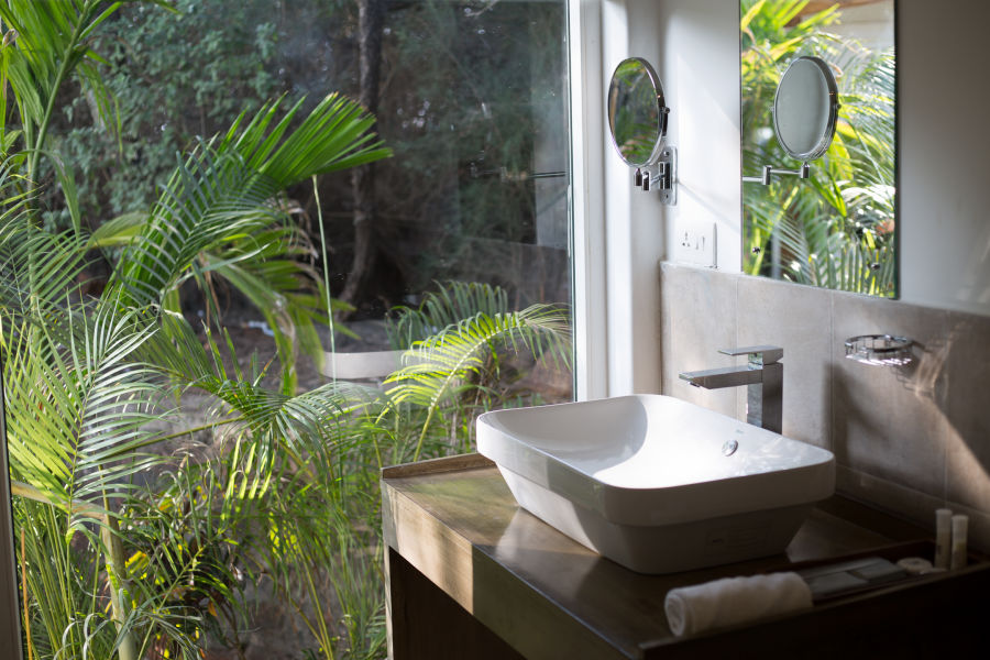 alt-text Spotless clean wash basin in the bathroom with a transparent french window and a beautiful garden view.