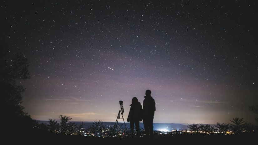 Two people standing along with telescope for star gazing