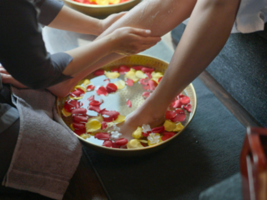 A foot soak with rose petals in a brass bowl, while a therapist massages a client