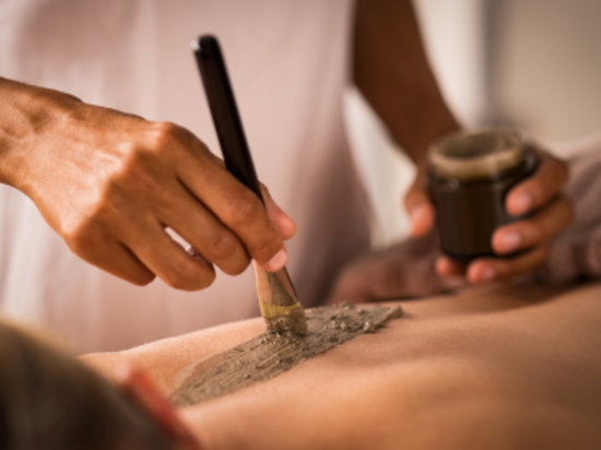 Hands applying a gray clay mask with a brush on someone