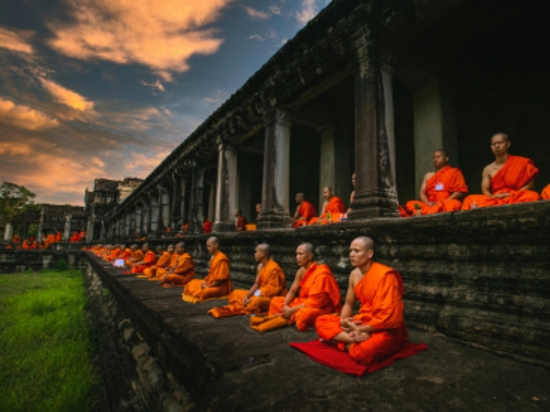 Monks in orange robes meditating in a historical temple at sunset.